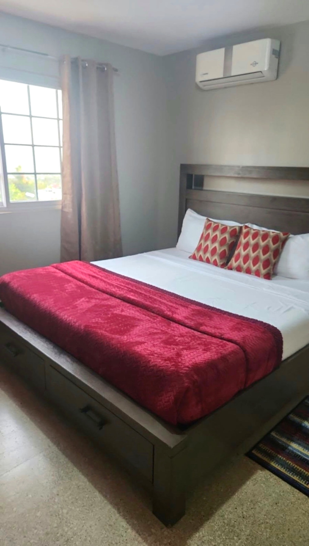 Condo bedroom with red bedding and a wall-mounted air conditioner